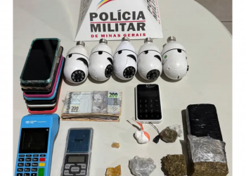 IPATINGA - Na manhã desta quinta-feira (19), a Polícia Militar de Minas Gerais (PMMG), por meio do 14º Batalhão de Polícia Militar (BPM), realizou uma operação de busca e apreensão no centro de Ipatinga. Durante a ação, três pessoas foram detidas: duas mulheres, de 39 e 20 anos, e um homem de 28 anos. A operação contou com o apoio aéreo de um helicóptero da 5ª Base Regional de Aviação do Estado (BRAVE), do Comando de Aviação do Estado (COMAVE), que auxiliou nas ações táticas. Materiais apreendidos Durante a operação, os policiais apreenderam diversos itens. Entre os materiais encontrados, estavam oito aparelhos celulares, seis câmeras de filmagem e quantidades significativas de drogas, como uma barra de maconha, duas buchas de maconha, um tablete de maconha e um papelote de cocaína. Além disso, foram encontrados itens como uma balança de precisão, uma faca, uma lâmina e R$ 1.177,00 em dinheiro. Também foram apreendidos 6 dólares americanos, 5 mil guaranis paraguaios, joias, como duas pulseiras douradas, 17 brincos e três anéis de prata, além de uma pedra de crack. A Polícia Militar segue com os trabalhos para investigar o envolvimento dos detidos com o tráfico de drogas e outros crimes na região.